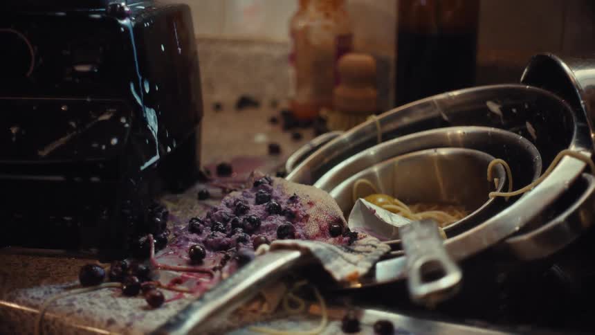 Blueberries and flour fall in slow motion onto a chaotic pile of dirty dishes on a messy kitchen counter