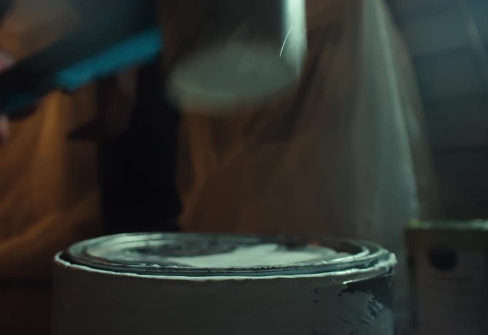 A close-up slow-motion shot of a painter using a rubber mallet to seal a can of white paint