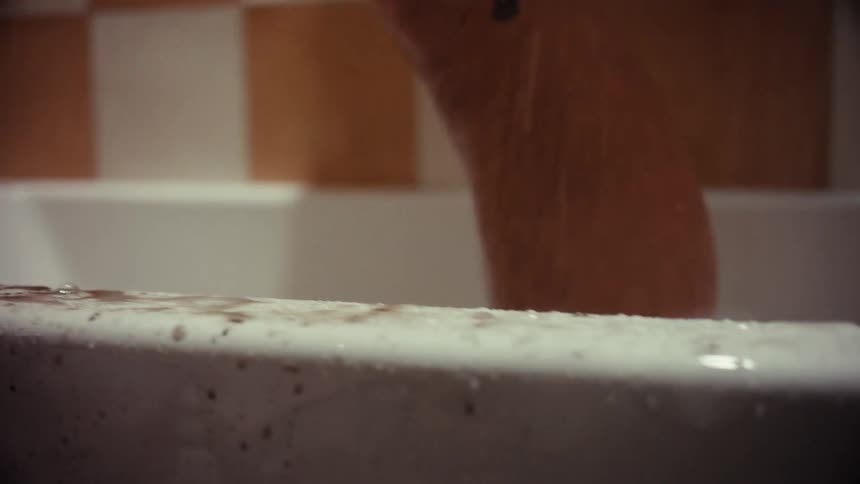 Blood and water mix and drip on the edge of a bathtub in a disturbing, cinematic horror scene