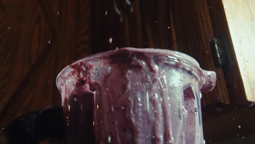 A close-up shot of a purple smoothie violently splashing out of an overflowing blender in dramatic slow motion