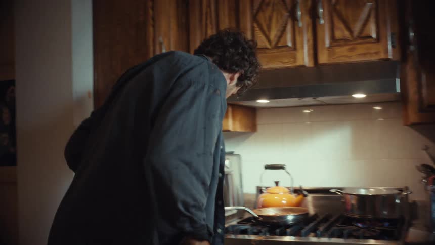 A father cooking in the kitchen playfully dances and reacts after his young son splashes him with water