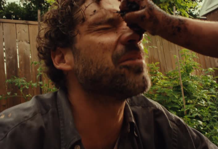 Playful son smears mud on his father's face during a messy play session in their backyard garden
