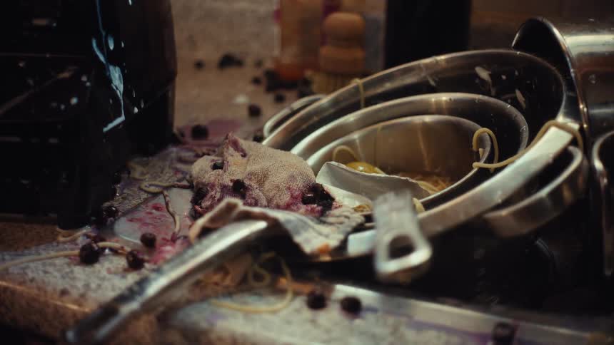 A gritty close-up of a messy kitchen sink piled high with dirty dishes, spilled spaghetti, and berries