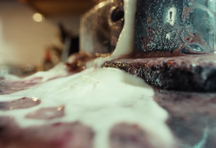 A macro shot of a white foamy substance being poured onto a purple berry mixture, creating a chemical reaction with vapor
