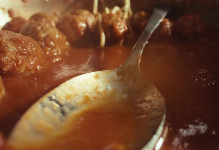 A spoon stirs a pot of delicious spaghetti and meatballs simmering in a rich, warm tomato sauce
