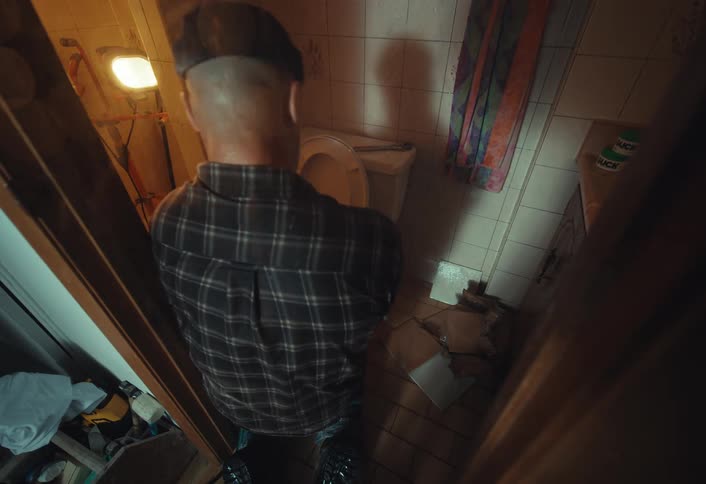 High-angle view of a sick man violently vomiting into the toilet in a disgusting, dimly lit bathroom