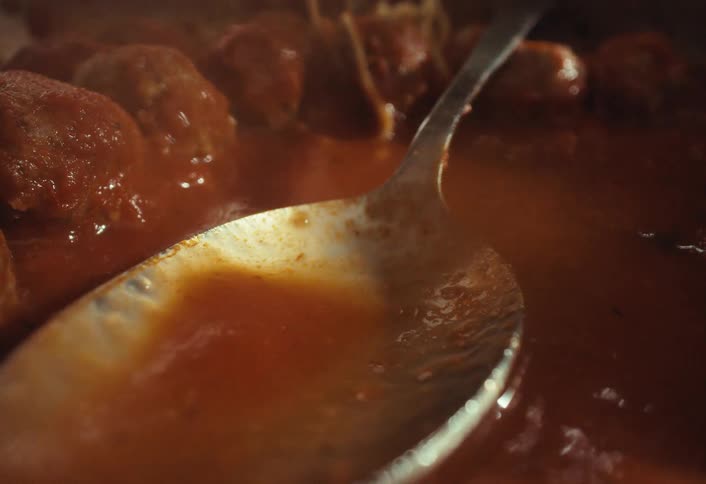 A spoon dips into a pot of savory meatballs simmering in a hearty tomato sauce