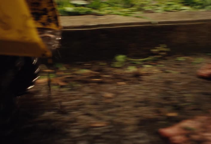 A joyful, muddy toddler plays with a yellow toy dump truck in a wet, dirty backyard garden