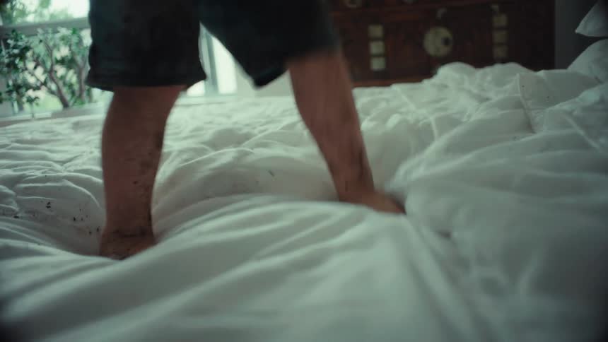 A happy but muddy little boy jumps on his parents' clean white bed before doing a somersault and getting tickled by his dad
