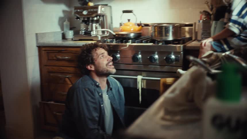 A joyful father and his young child have a messy spaghetti food fight in their kitchen, laughing and bonding together