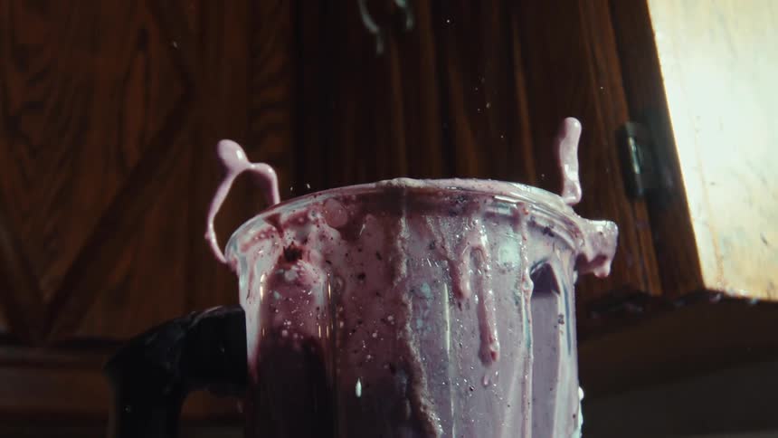 A messy berry smoothie overflows and erupts from the top of a blender in an epic slow-motion splash