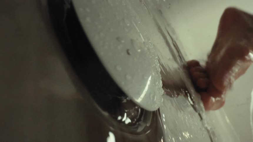 Low-angle close-up of feet being washed in a bathtub with water running down the overflow drain