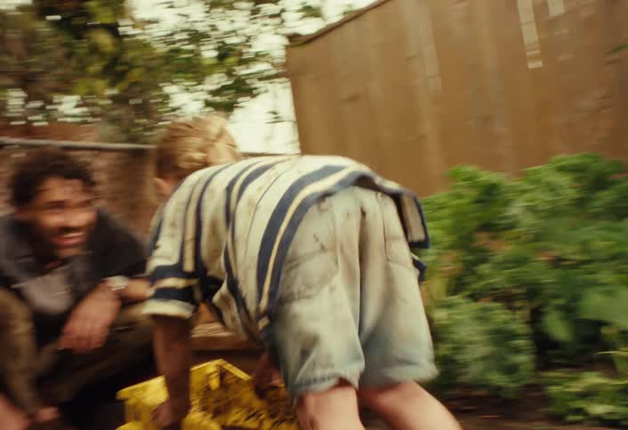 A muddy toddler happily plays with a toy dump truck in the backyard garden with his father