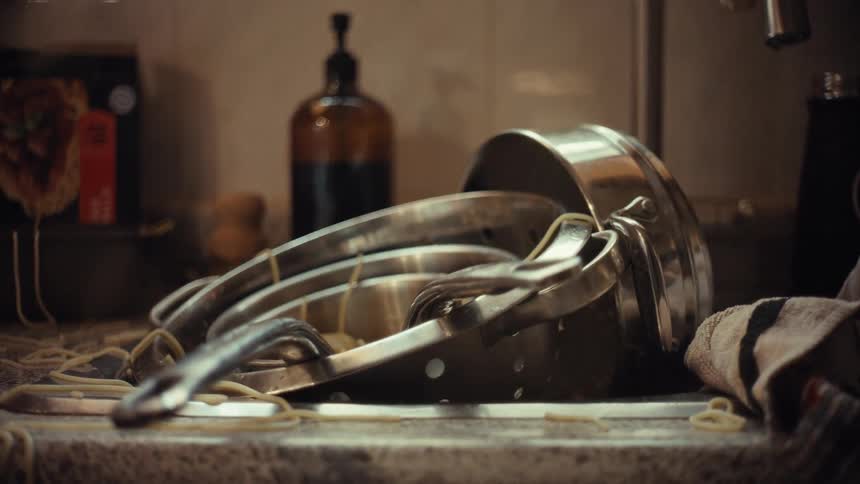 A slow zoom out reveals a messy kitchen sink piled high with dirty dishes and uncooked spaghetti after a cooking mishap