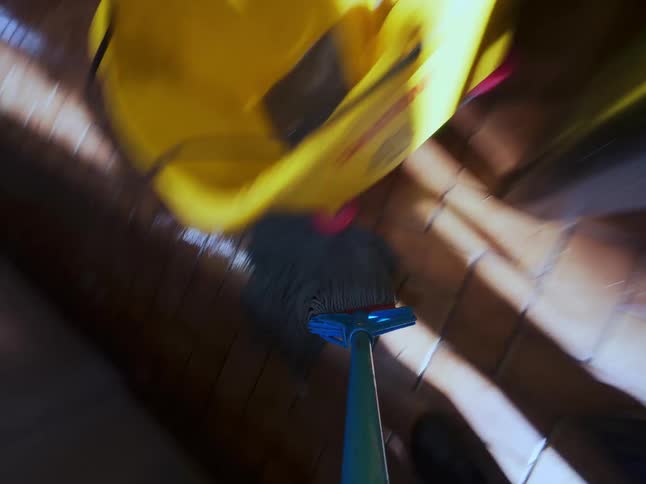 A dynamic first-person perspective of someone mopping a tiled floor in a commercial kitchen or utility room