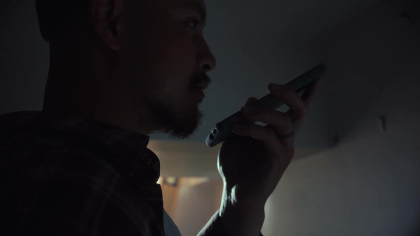 A man in a dark room makes a serious phone call on speaker in slow motion