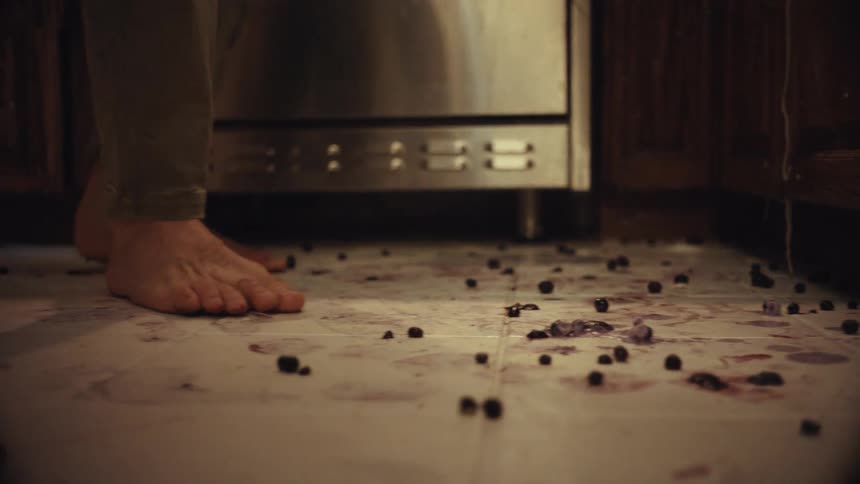 Bare feet step on and crush spilled blueberries all over a messy kitchen floor
