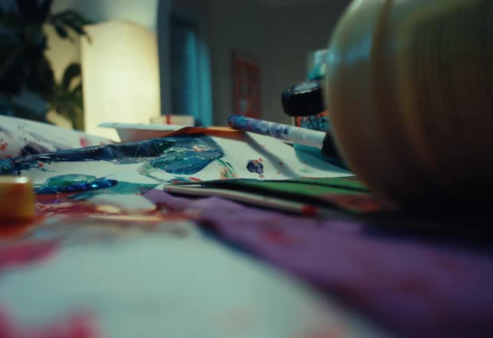 A close-up of a messy art table where a pumpkin is rolled into frame for Halloween painting