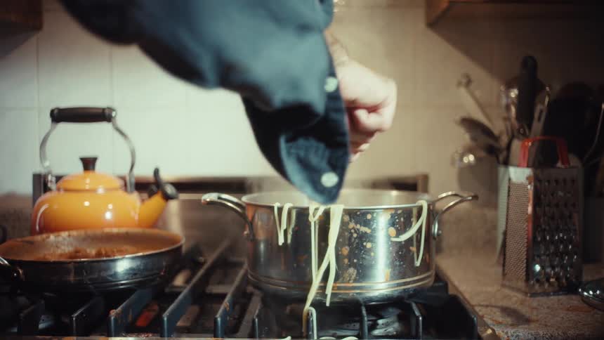 Slow motion shot of a person lifting steaming hot spaghetti from a messy pot on a stove
