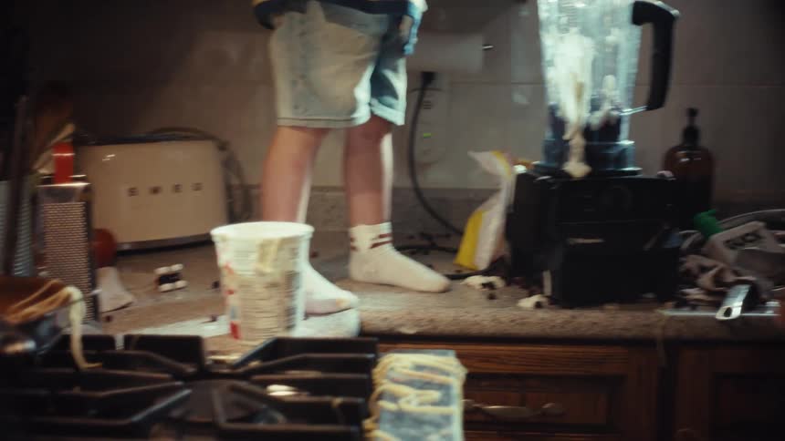A father and his young son have fun making a very messy smoothie together in a sunlit kitchen
