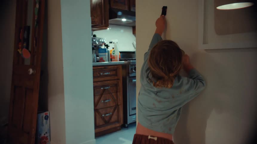 A messy little girl dips her paintbrush and begins to creatively paint on the white wall of her home