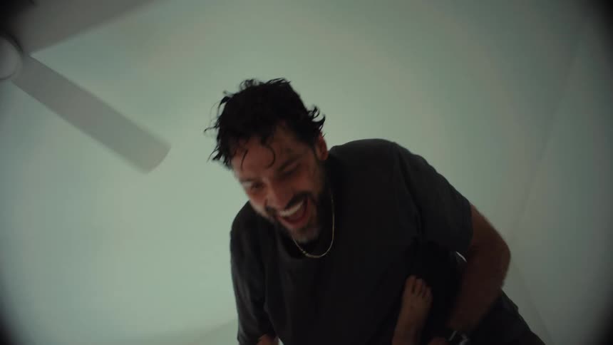A father playfully holds his laughing son upside down and swings him around on a bed in slow motion