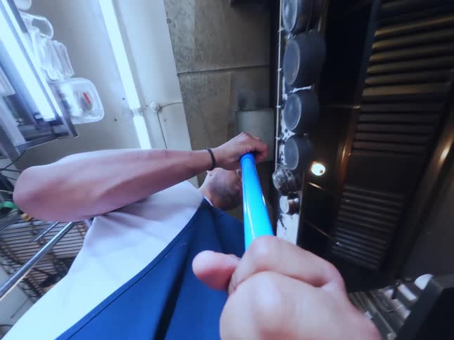Point-of-view shot from a broom's perspective as a man in an apron sweeps a commercial kitchen floor