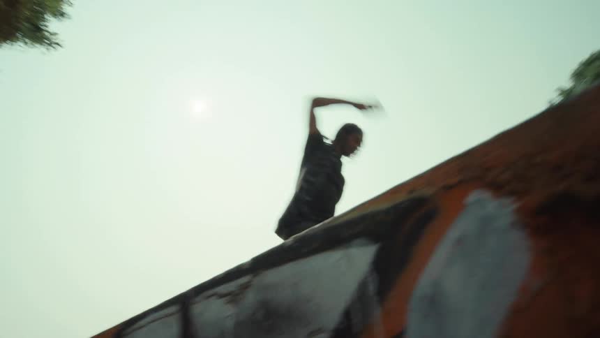 A silhouetted freerunner gracefully balances and runs along the top of a graffiti-covered urban wall against a bright, hazy sky