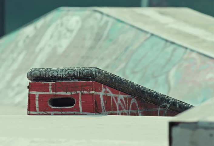 A slow zoom out reveals a graffiti-covered ramp and rail at an empty urban skatepark