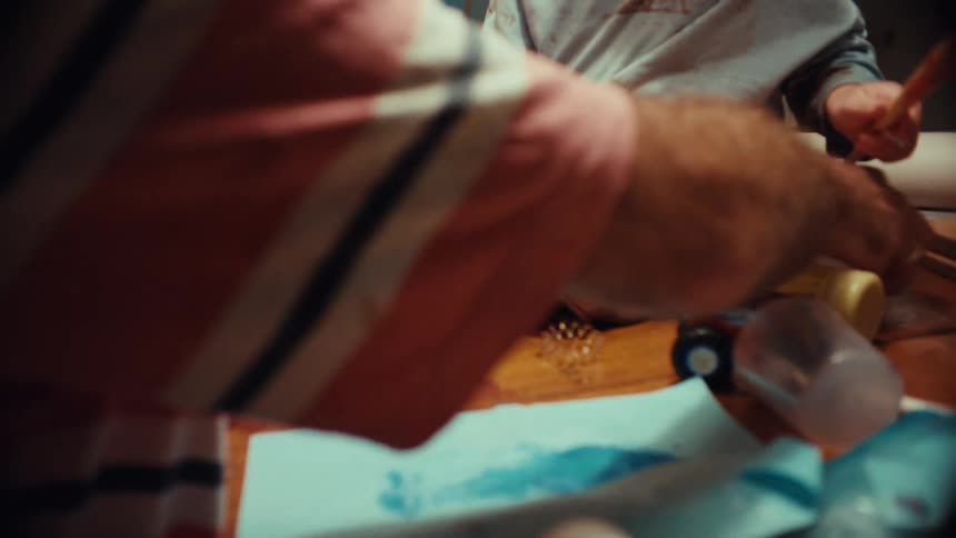 A father and his young son playfully paint on each other's legs during a messy and joyful art session at home