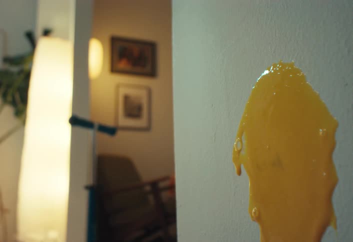A yellow egg yolk is thrown against a white interior wall and slowly drips down in a close-up shot