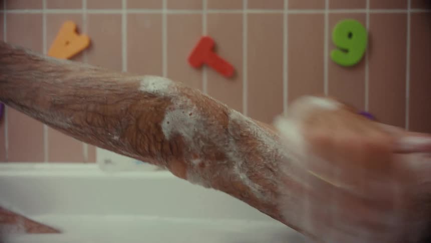 A close-up shot of a man with paint on his face washing soap onto his arm in a bubble bath