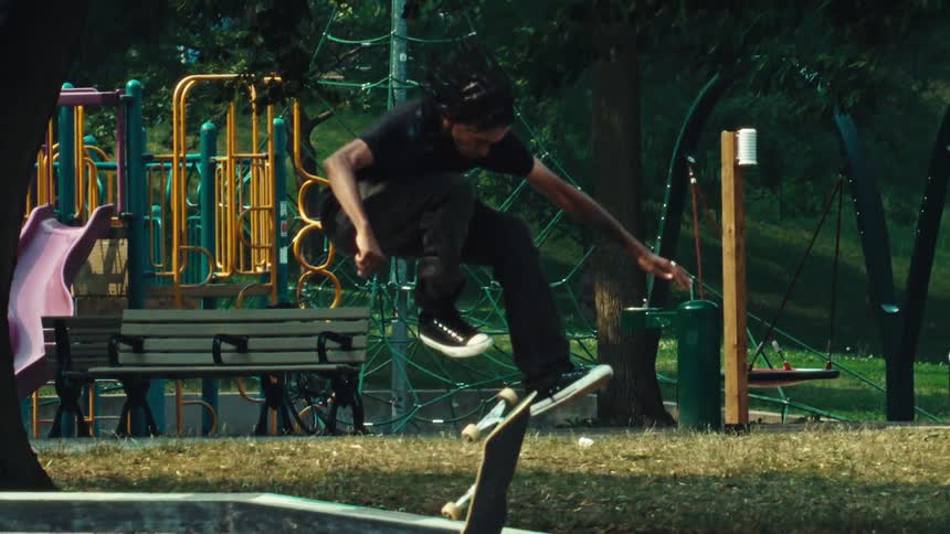 A skateboarder at a park attempts a kickflip to boardslide on a rail in dramatic super slow motion