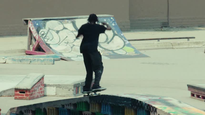 Slow motion view of a skateboarder landing a kickflip off a ramp at an urban skatepark and celebrating