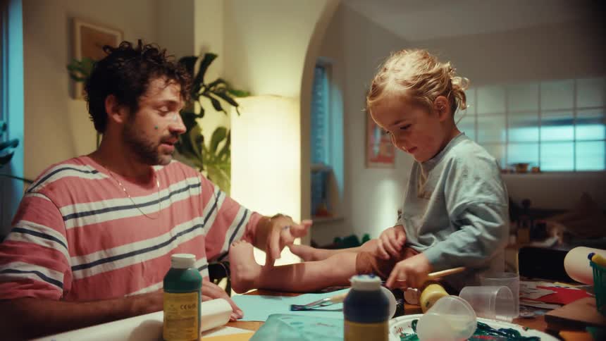 A happy father and his toddler get messy with paint, laughing and playing together during an arts and crafts session at home