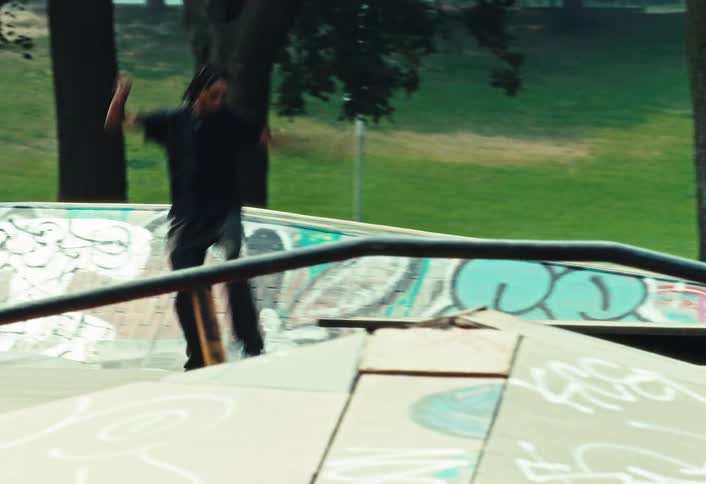 A skateboarder in slow motion rides up a ramp and skillfully grinds along a box at an outdoor park