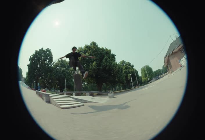 Fisheye slow-motion shot of a stylish skateboarder landing a kickflip down a set of stairs at an outdoor skatepark on a sunny day