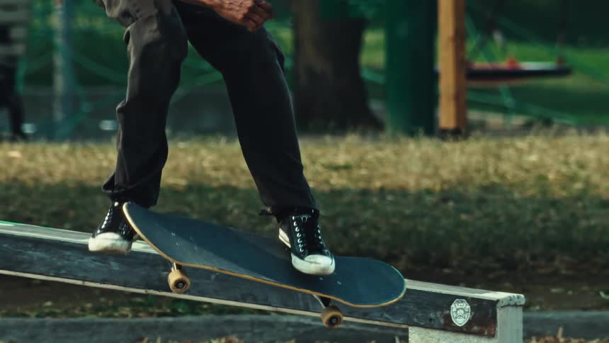 A skateboarder performs a kickflip and lands on a rail to grind in super slow motion at an outdoor skatepark