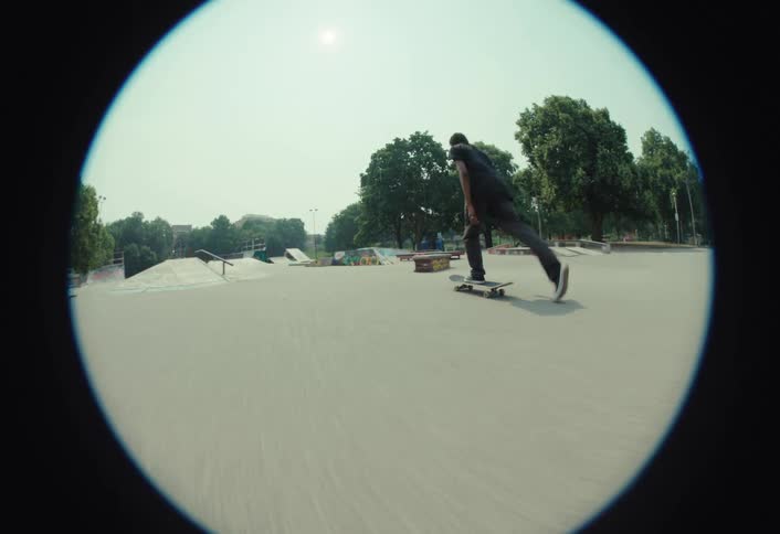 Fisheye slow-motion shot of a skateboarder dropping into a ramp and performing a trick at an outdoor skatepark