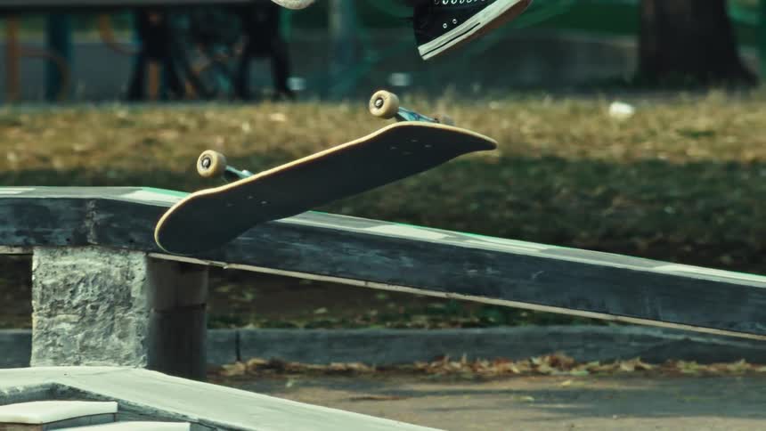A skateboarder performs a kickflip in super slow motion at a skatepark, with the camera tilting up to reveal the person mid-air