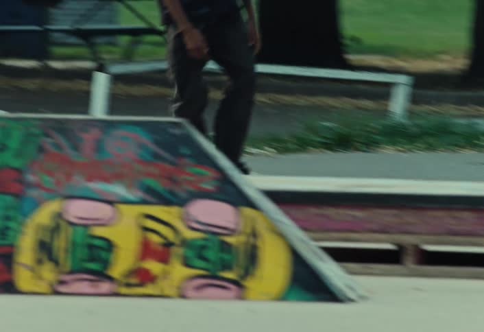 Slow motion side view of a focused skateboarder cruising through a skatepark and landing a kickflip trick