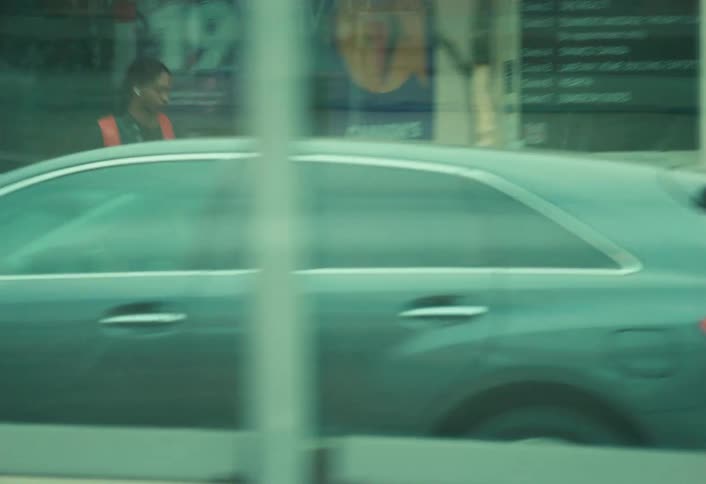 A young man with a backpack carrying a jug walks along a city sidewalk in a cinematic tracking shot