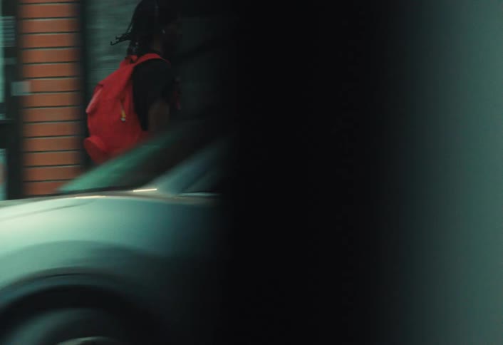 Slow-motion side view of a young man with a red backpack skateboarding down a city sidewalk