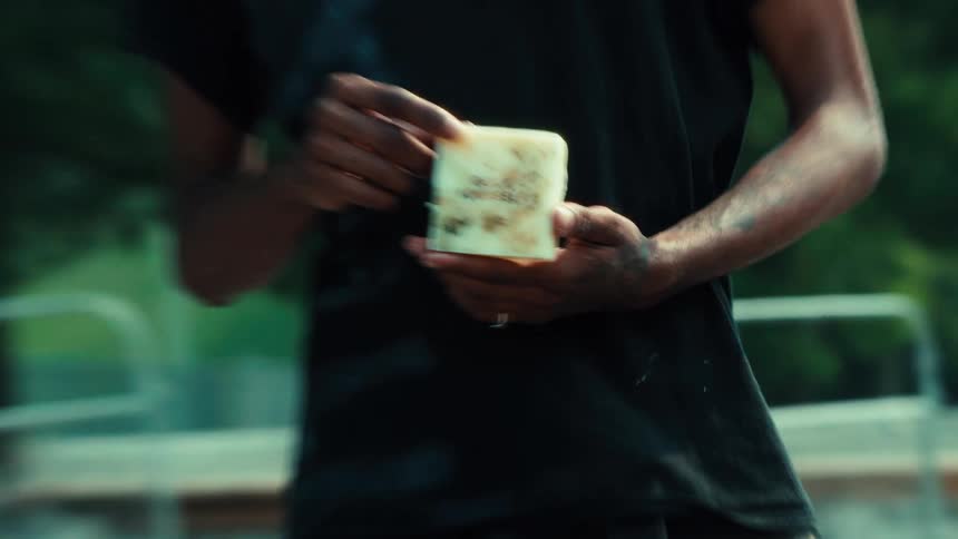 A close-up reveals a person with dirty hands holding a bar of handmade soap that reads 'Guck Yourself'