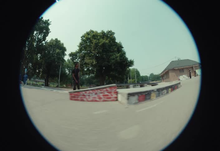 Slow motion fisheye shot of a young man skateboarding at a park, successfully landing a stylish kickflip over a gap