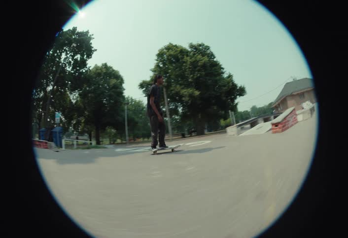 Fisheye lens follows a skateboarder in slow motion as he flawlessly executes a kickflip over a gap at a skatepark