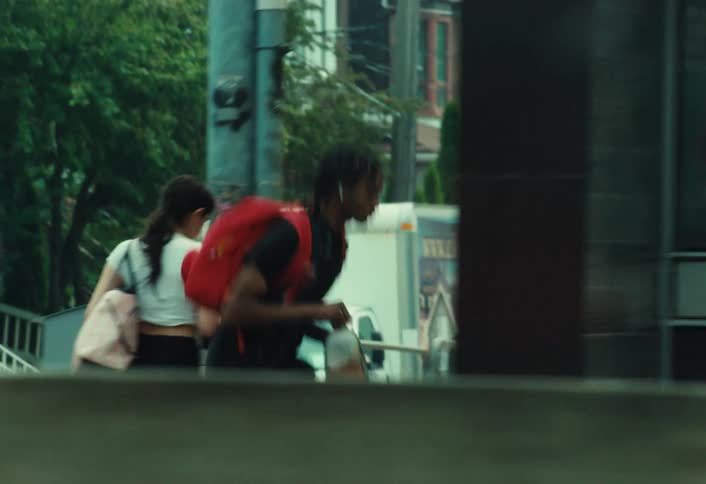 Side-view tracking shot of a young man with a red backpack skateboarding down a busy city street
