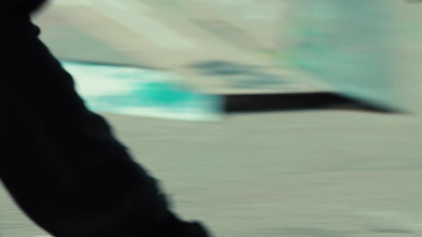 A slow-motion close-up of a skateboarder's feet performing a grind trick on a rail in a skatepark