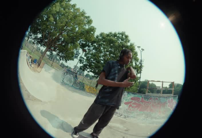 A skateboarder cruises through a graffiti-covered skatepark before revealing his bloody, scraped elbow and wiping it on the fisheye lens