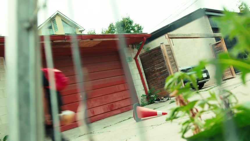 A skateboarder with a red backpack performs an ollie trick over a traffic cone in an urban alleyway